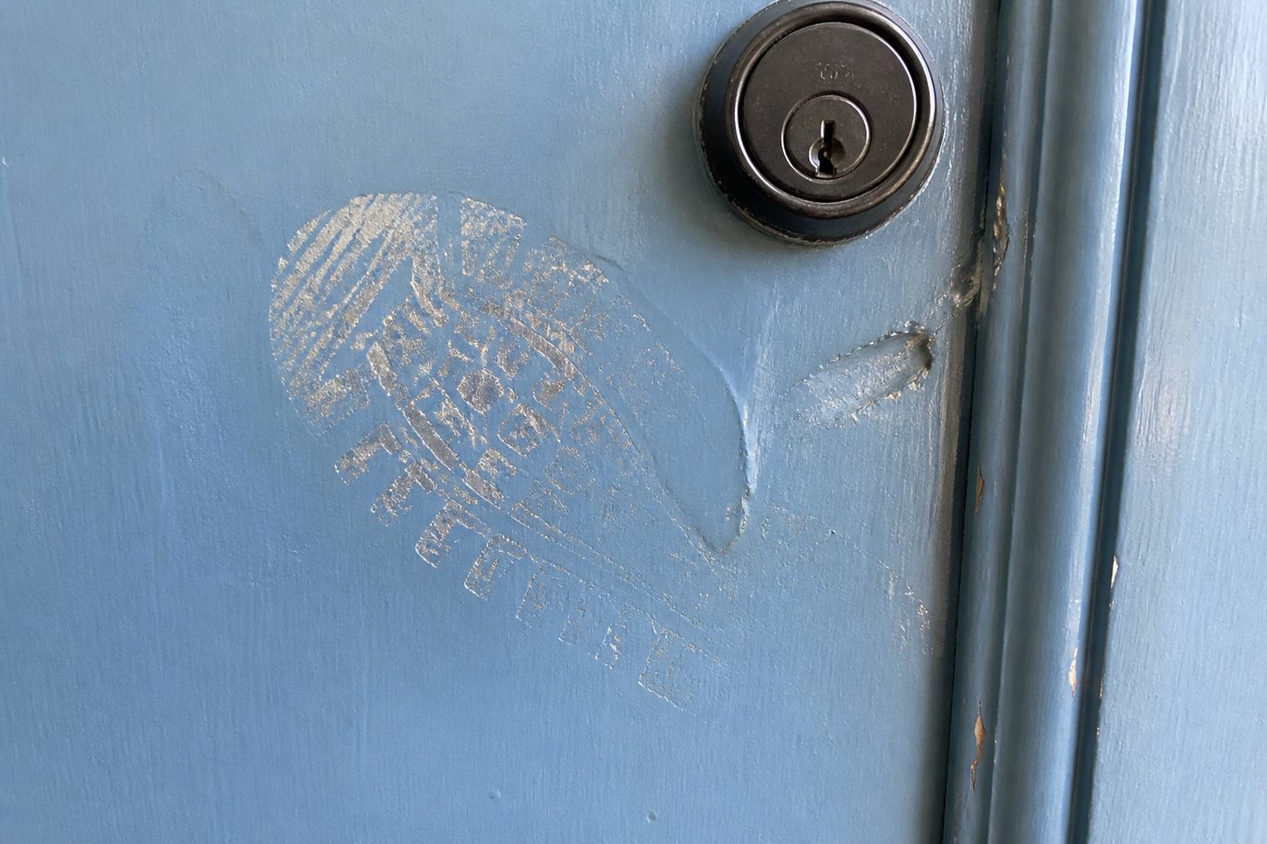 A boot print scuffed into the paint of a front door beside the lock