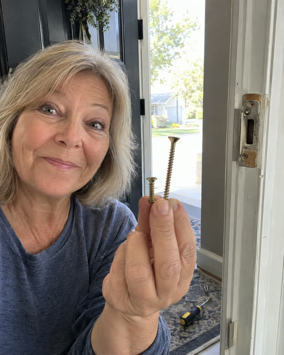 A reader in her doorway holding up the long screw she just took out of her door frame