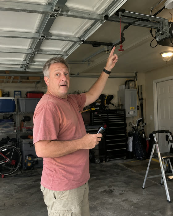 A reader in his garage pointing up at the emergency release cord on the opener