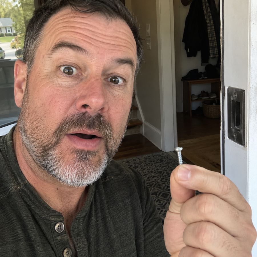 A man holding up the very short screw he pulled from his door